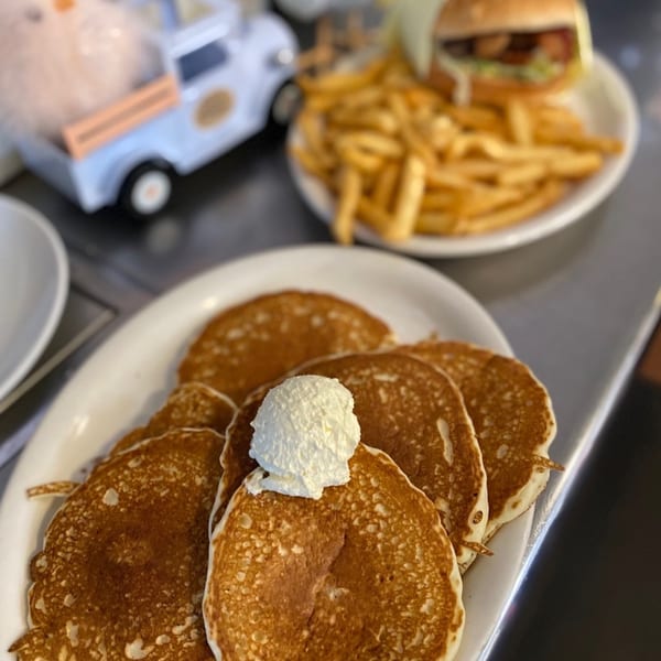 A plate of pancakes with whipped cream, a burger, and fries at Old Time Drive In.