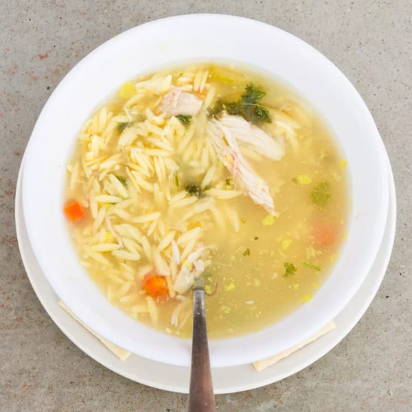A white bowl of Old Time Drive In's chicken noodle soup with orzo, carrots, and parsley.