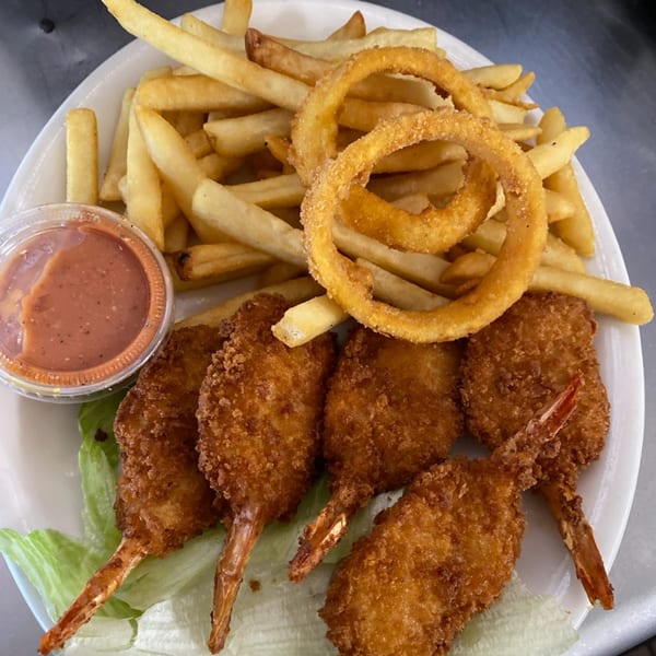 Old Time Drive In's fried shrimp and onion rings with fries and dipping sauce on a white plate.