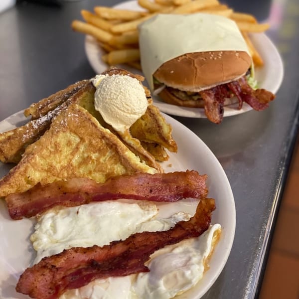 Plates of diner food, including French toast with bacon and eggs, and a burger with fries.