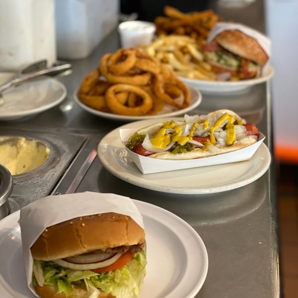 Diner counter with a hot dog, burger, onion rings, and fries on white plates.