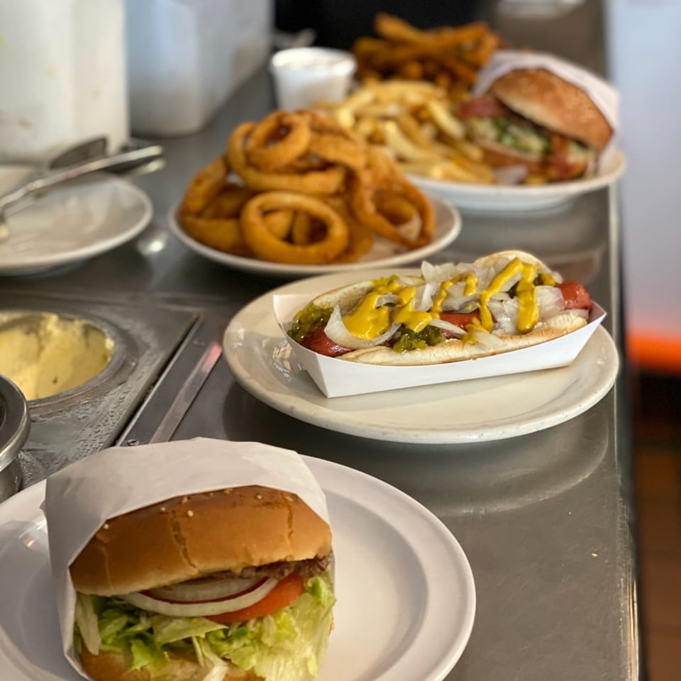 Diner counter with a hot dog, burger, onion rings, and fries on white plates.