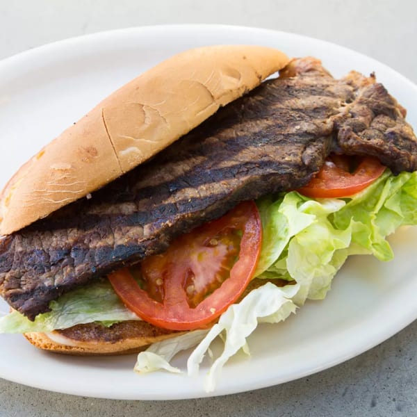 A grilled steak sandwich with lettuce and tomato on a white plate from Old Time Drive In.